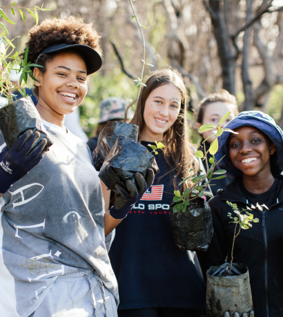 Students smiling and holding saplings on regeneration project