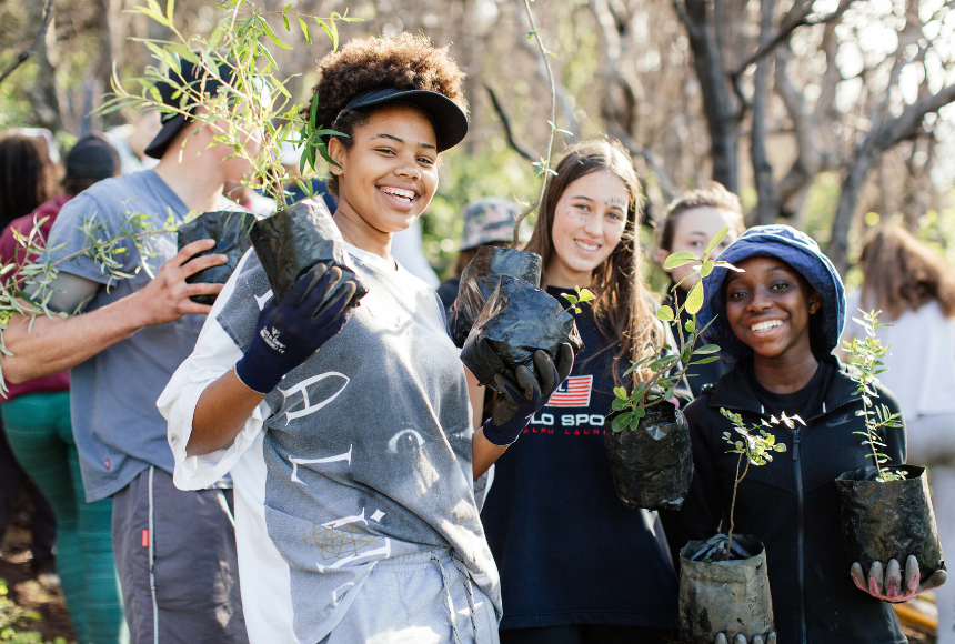 Students smiling and holding saplings on regeneration project