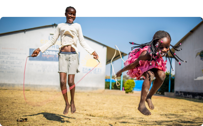 Two Zambian girls playing in playground with skipping ropes. One girl is wearing a bright pink dress