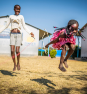 Two Zambian girls playing in playground with skipping ropes. One girl is wearing a bright pink dress